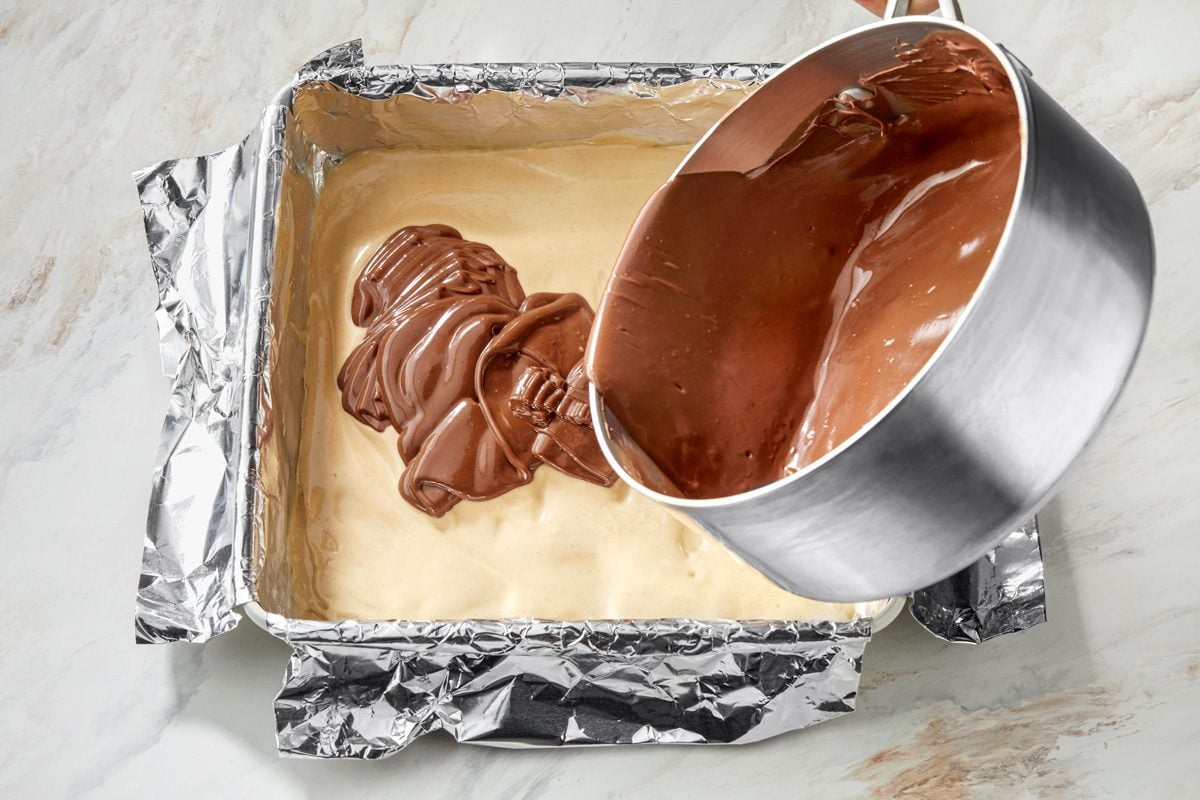 Pouring a smooth chocolate mixture over a creamy vanilla layer, creating a layered effect
