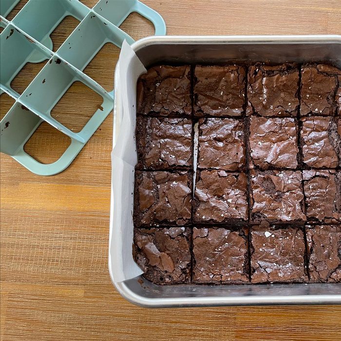 Metal pan of cooked brownies with a grid slicer to the top right