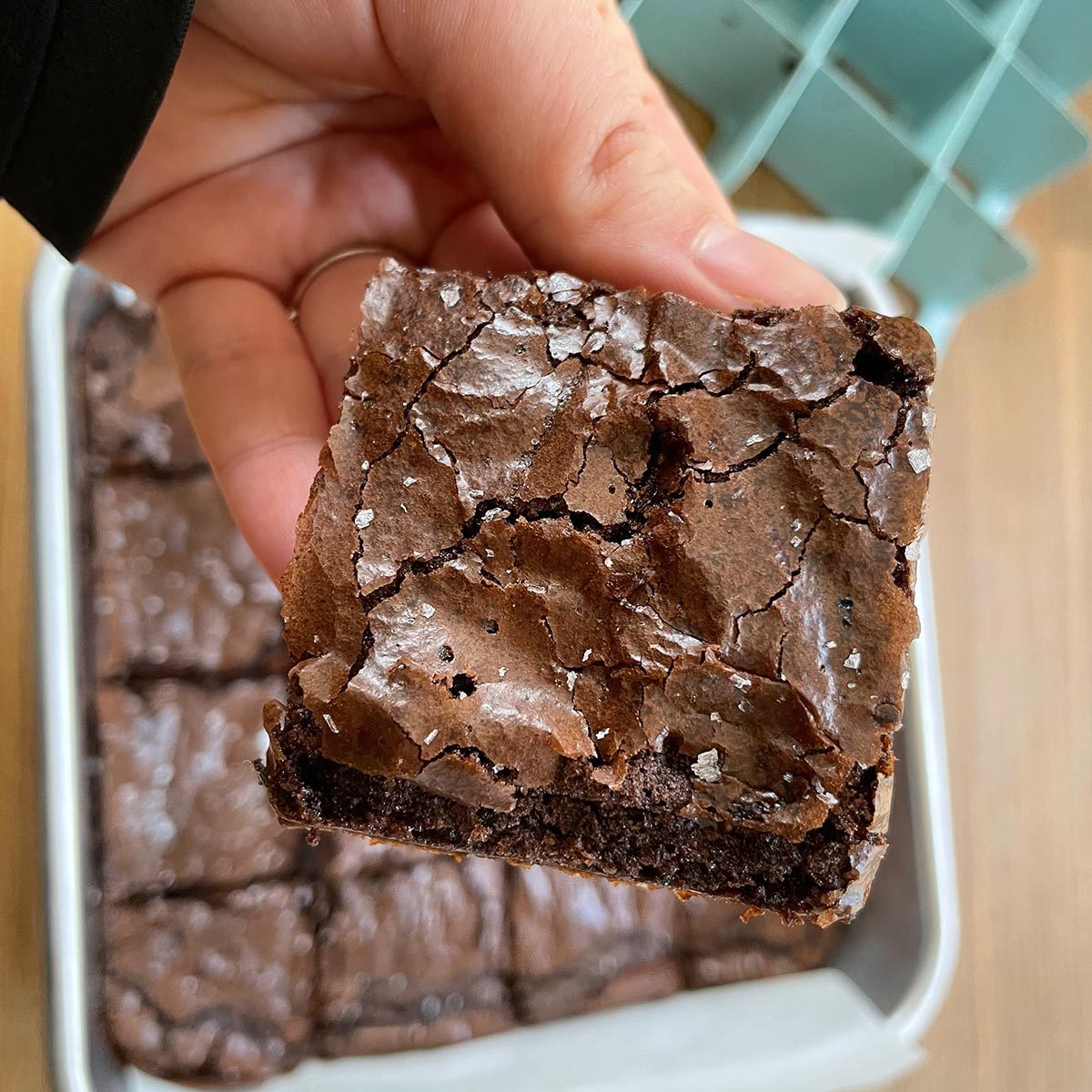 Close-up of hand holding a brownie with a pan of brownies in the background