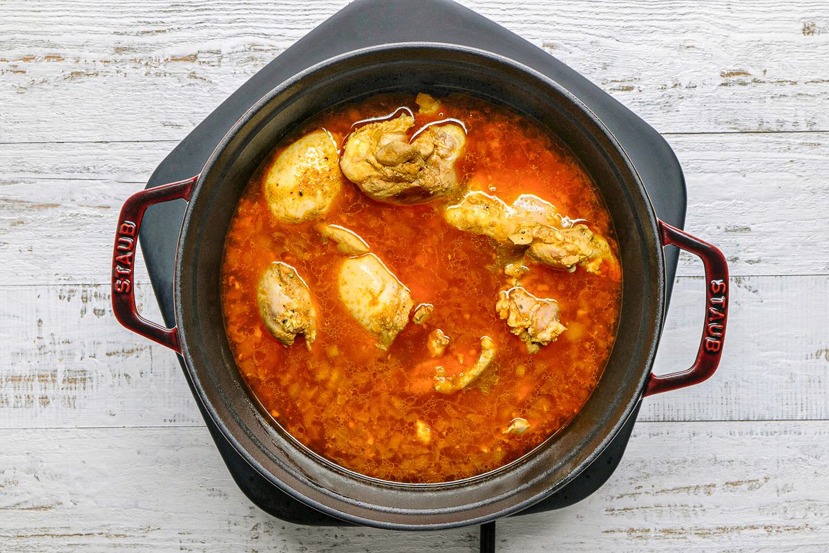 chicken being cooked with curry in dutch oven