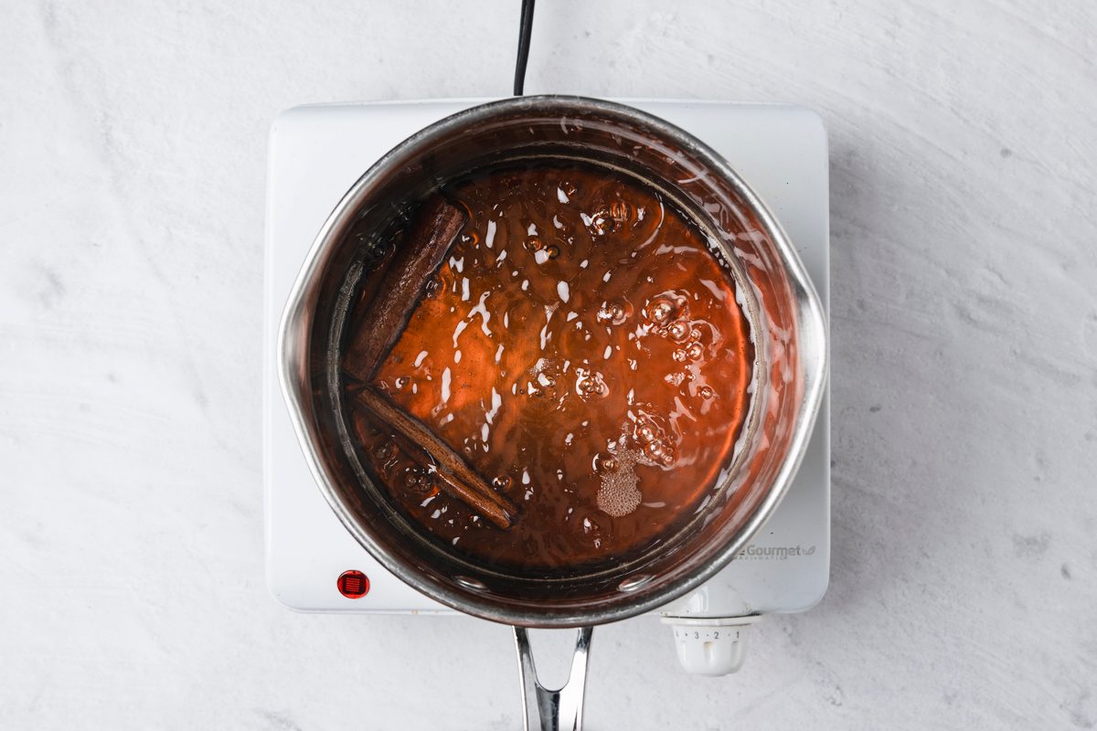 Overhead shot of a small saucepan over medium-high heat; combine apple juice or cider and brown sugar; stir; add cinnamon stick; bring to a boil; then reduce heat and simmer 8-10 minutes or until sugar is dissolved and mixture has reduced slightly; Remove from heat and add vanilla; let cool; induction; marble surface;