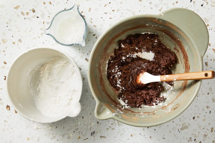 Overhead shot of a small bowl combine flour; baking powder and salt; Alternate adding the dry mixture and milk into the sugar mixture; stir until batter is smoot; spatula; marble surface;
