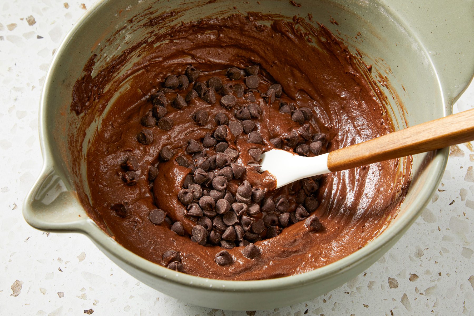 Close shot of fold in chocolate chips; spatula; marble surface;