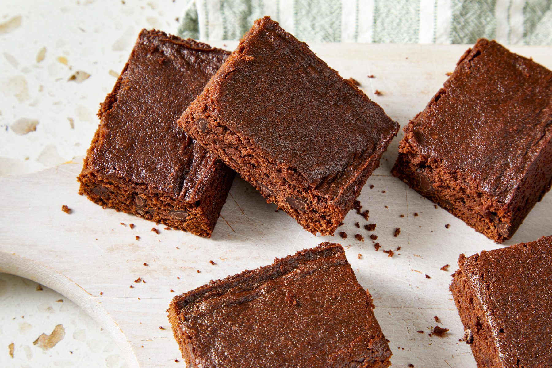 Overhead shot of Eggless Brownies; cut into pieces and served on white wooden tray over a napkin; all set on a marble surface;