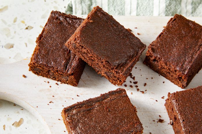 Overhead shot of Eggless Brownies; cut into pieces and served on white wooden tray over a napkin; all set on a marble surface;