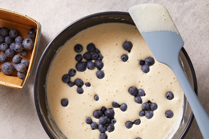A mixing bowl filled with pancake batter and fresh blueberries, with a spatula resting on the edge.