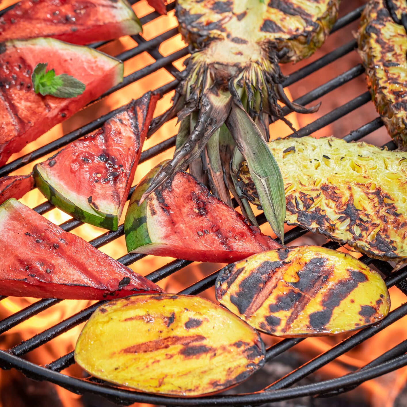 Roasted watermelon and pineapple with fire on grill grate.