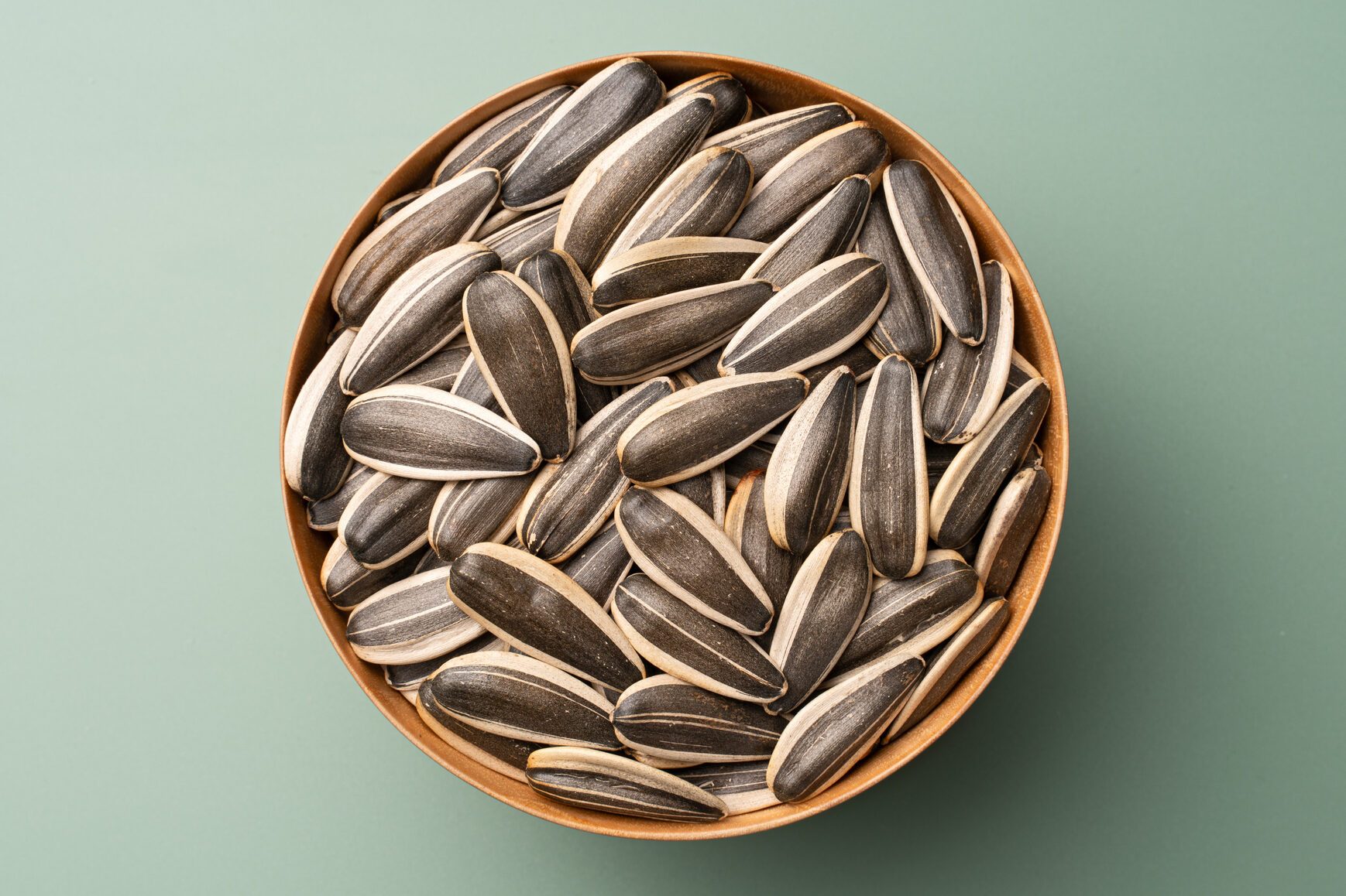 Whole Sunflower Seeds in Wooden Bowl on Green Background