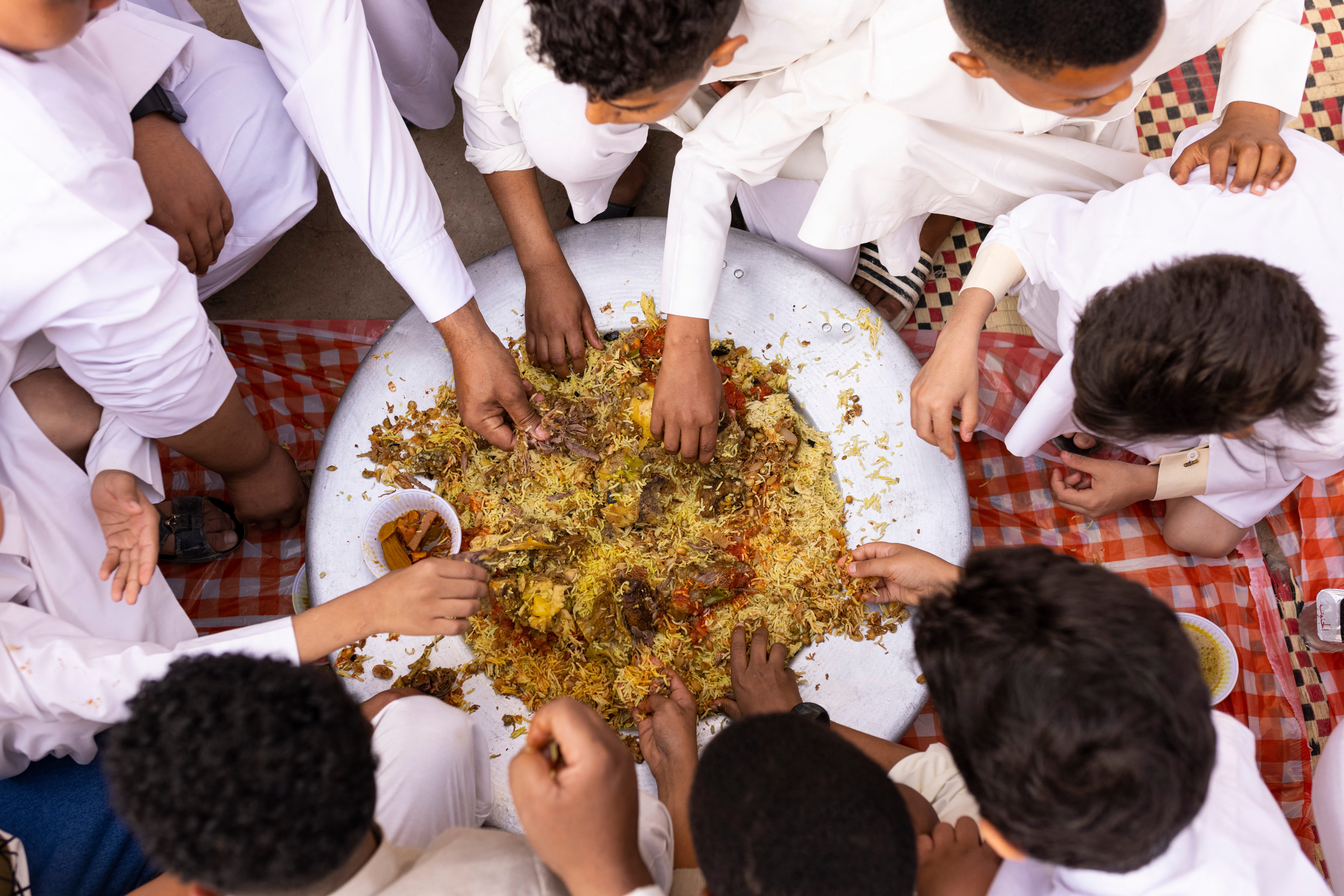 Birds eye view of several children grabbing helpings from a large plate of a rice dish
