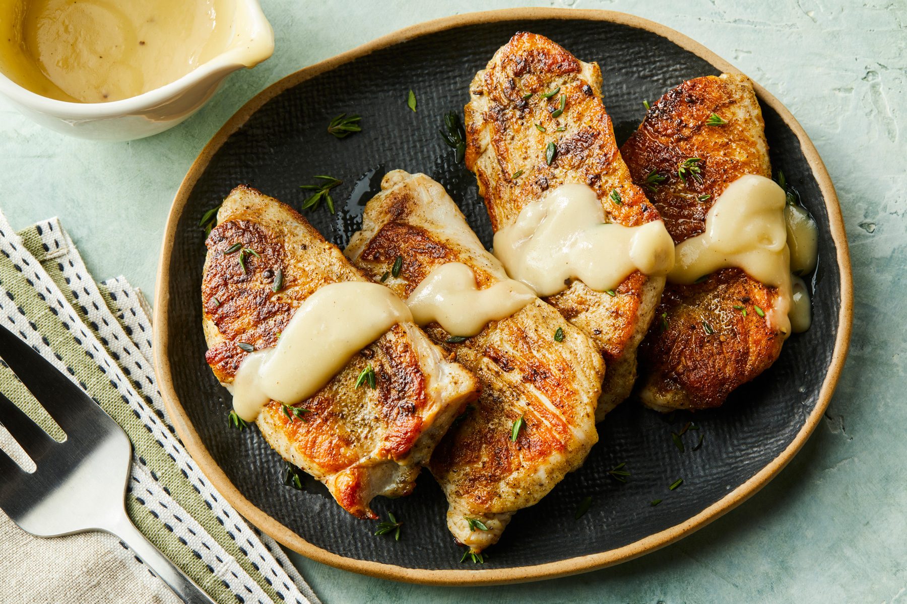3/4 angle view shot of Turkey Cutlets with Pan Gravy; served on a large platter; spread gravy over turkey cutlets; flat spoon placed over a napkin; all set on a light green surface;