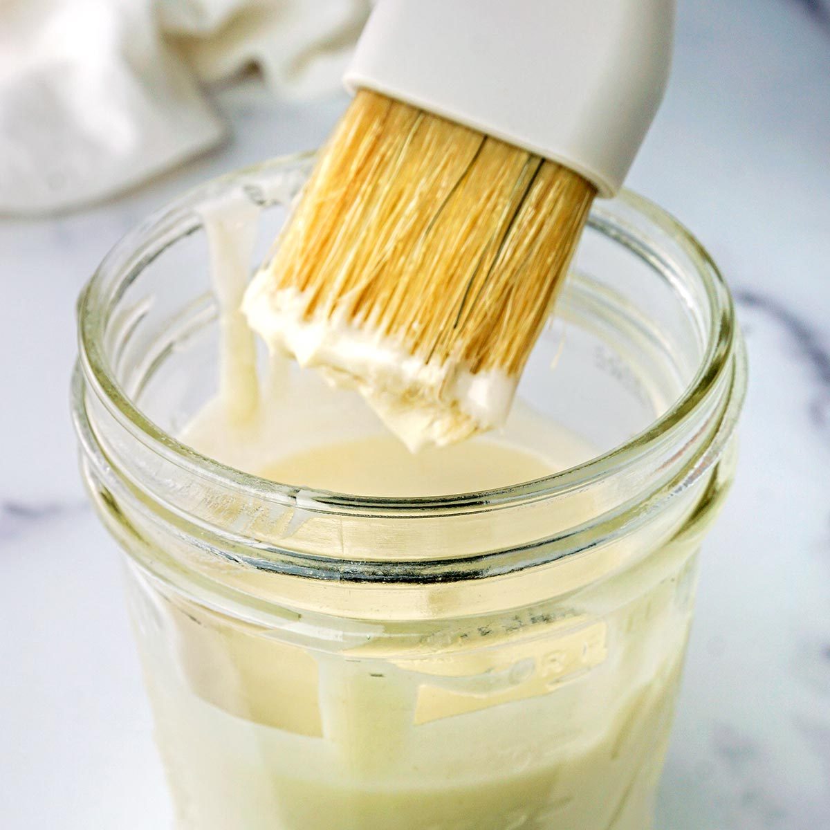 Homemade cooking spray dripping from a pastry brush into a mason jar