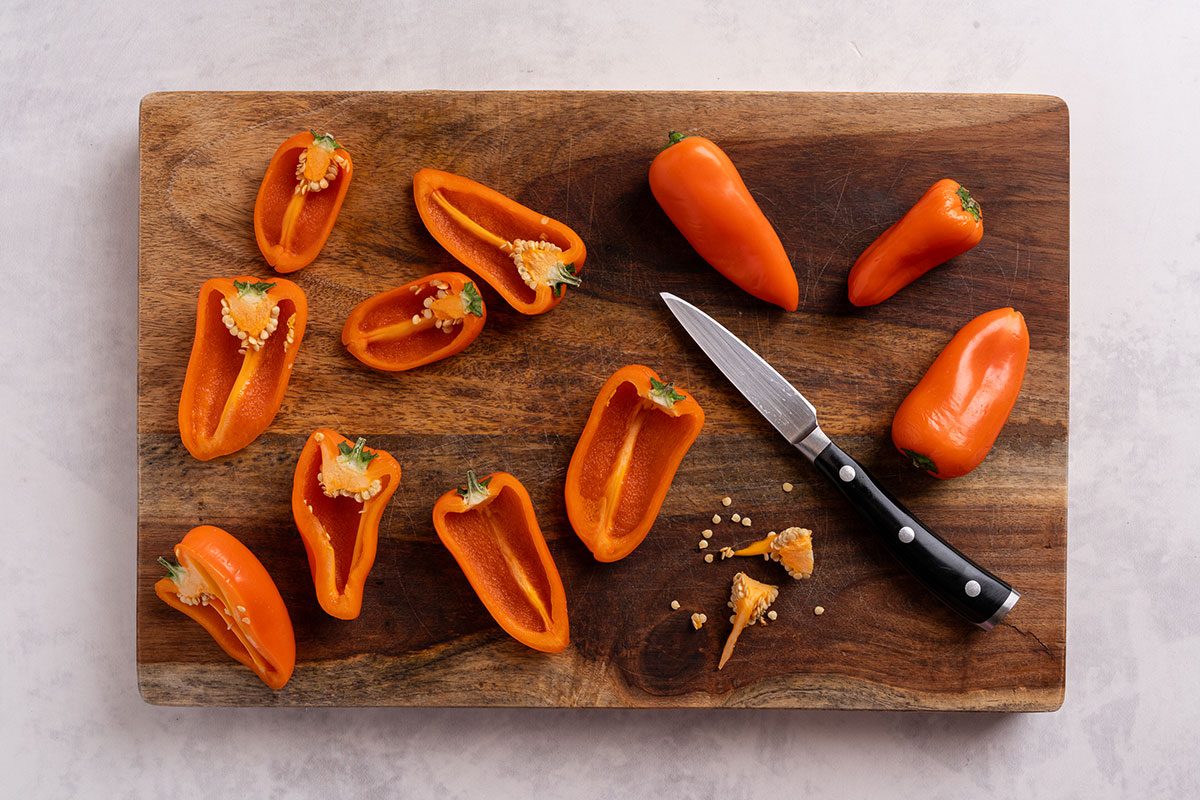 Orange bell peppers halved on a wooden cutting board with a paring knife