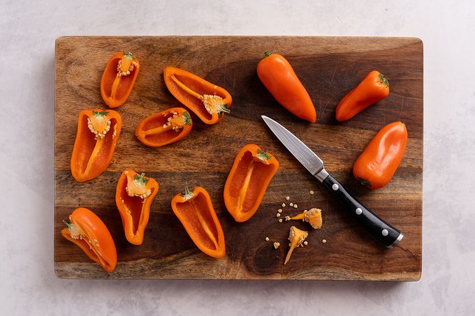 Orange bell peppers halved on a wooden cutting board with a paring knife
