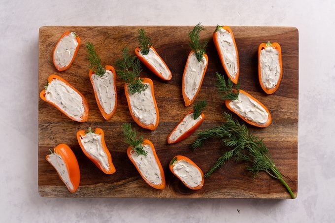 Stuffed halves of orange bell peppers with a cream cheese dip and dill sprigs on a wooden cutting board