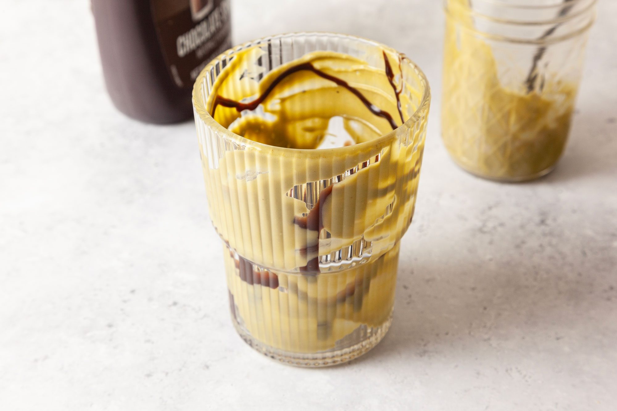 Use a spoon to smear 1/2 of the mixture onto the inside of a tall glass in an abstract pattern and add a few drizzles of chocolate syrup inside the glass