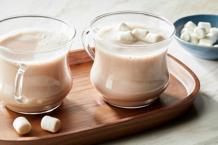 Table view shot of Fluffy Hot Chocolate; served in glass mugs on a wooden tray; accompanied by a bowl of marshmallows; set on a marble surface