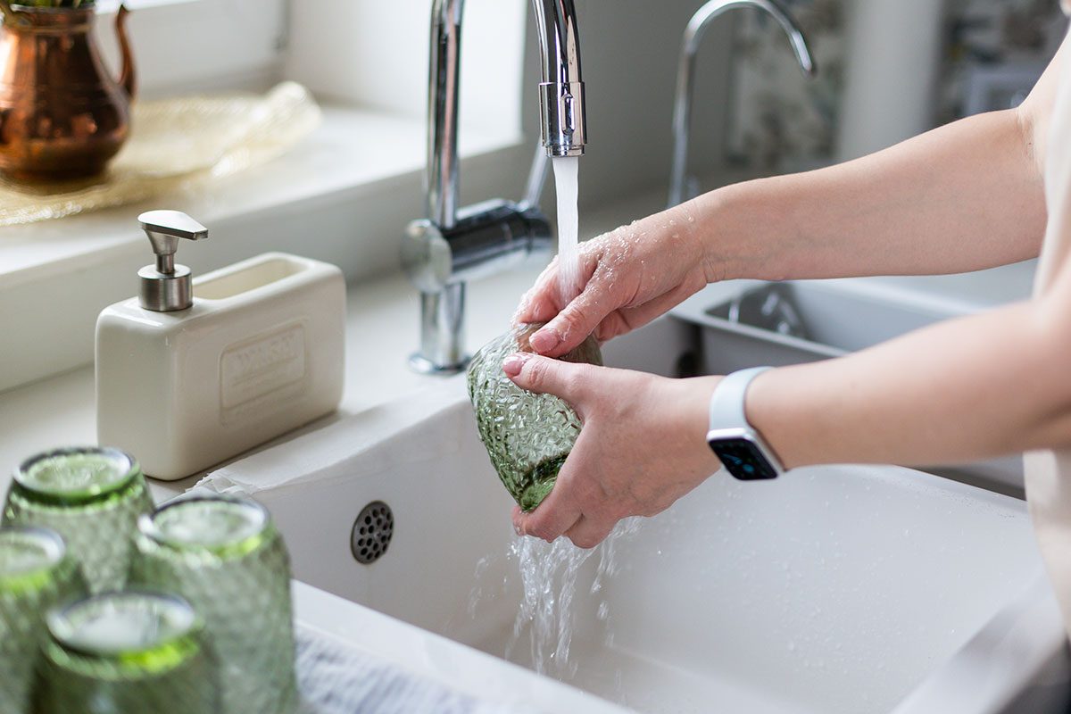 Female hand washeing a glass under running water in the kitchen