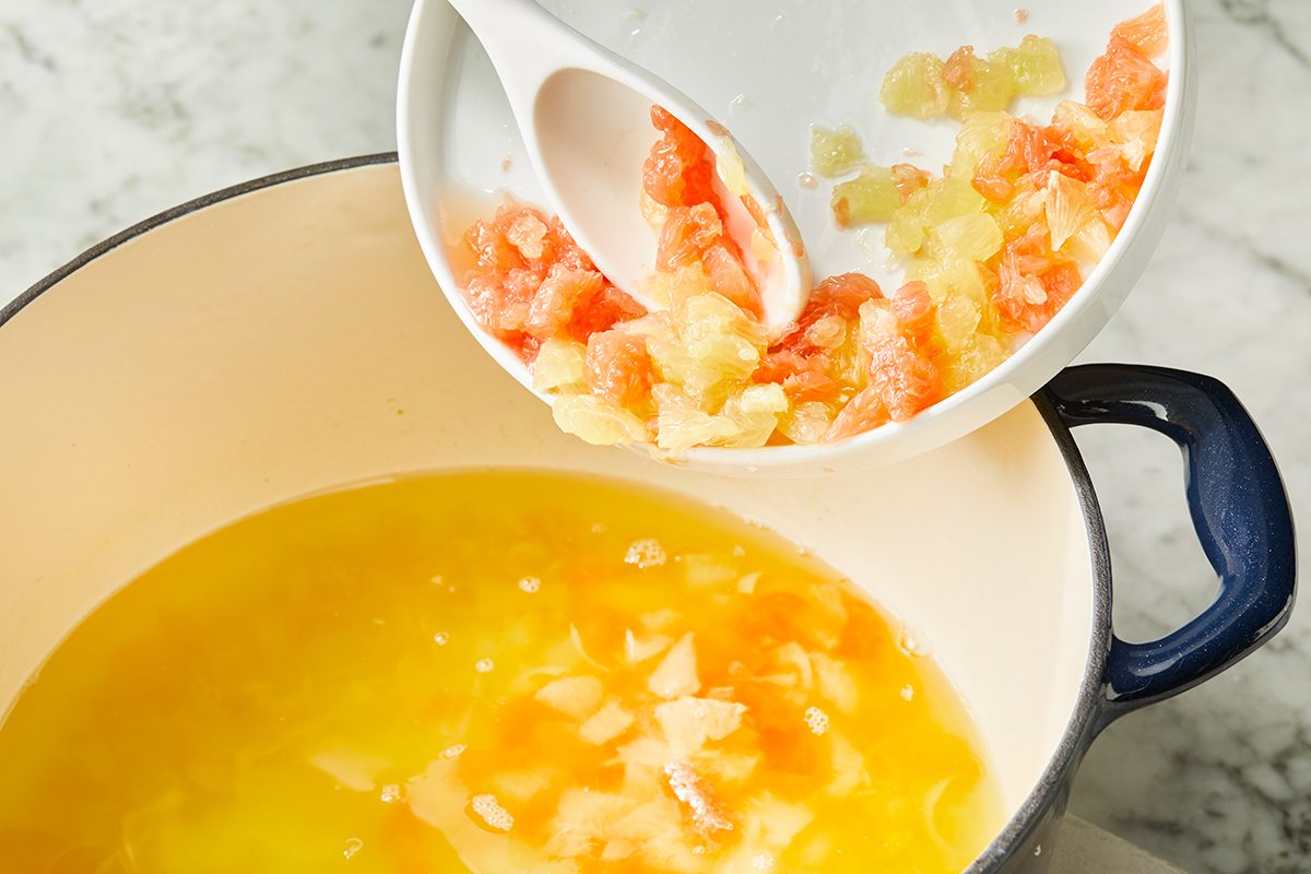 A white bowl with chopped onions and tomatoes is being poured into a large pot containing melted butter or oil on a marble countertop.