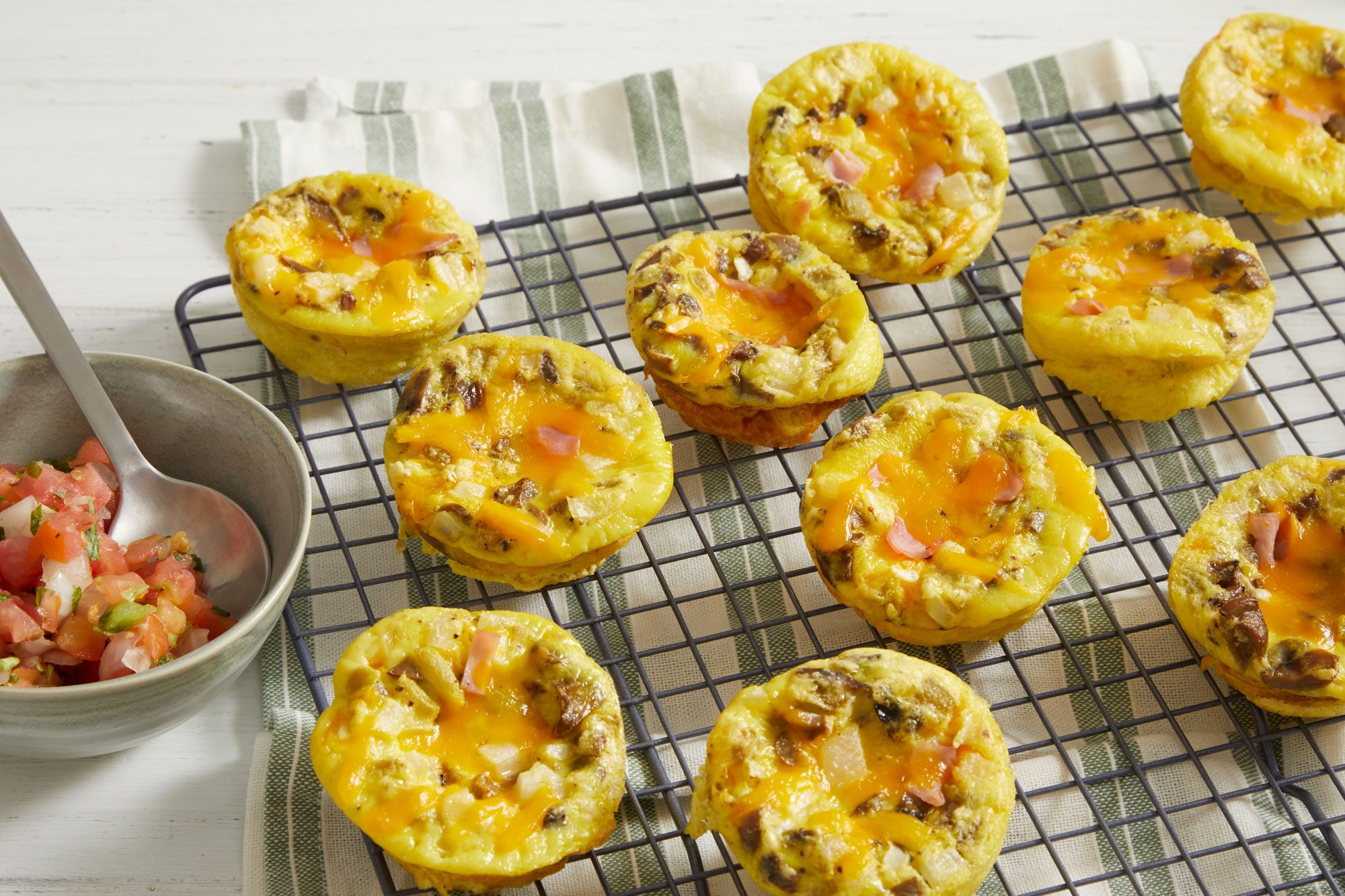 Table view shot of Muffin-Tin Scrambled Eggs; transfer on wire rack over a napkin; serve with pico de gallo; all set on white wooden surface