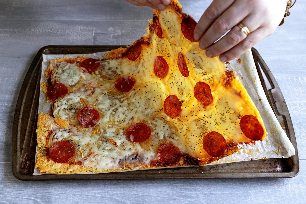 Hand bending the onion "pizza" up from its baking sheet, showing its translucent layer of onions
