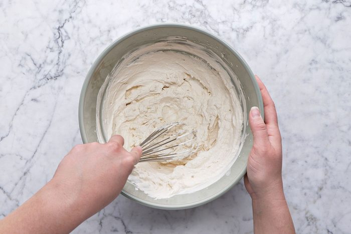 Overheda shot of Place heavy whipping cream; espresso powder; confectioners’ sugar and vanilla extract in a large bowl; Whisk until soft peaks form; set aside; whisk tool; all set on a marble textured surface