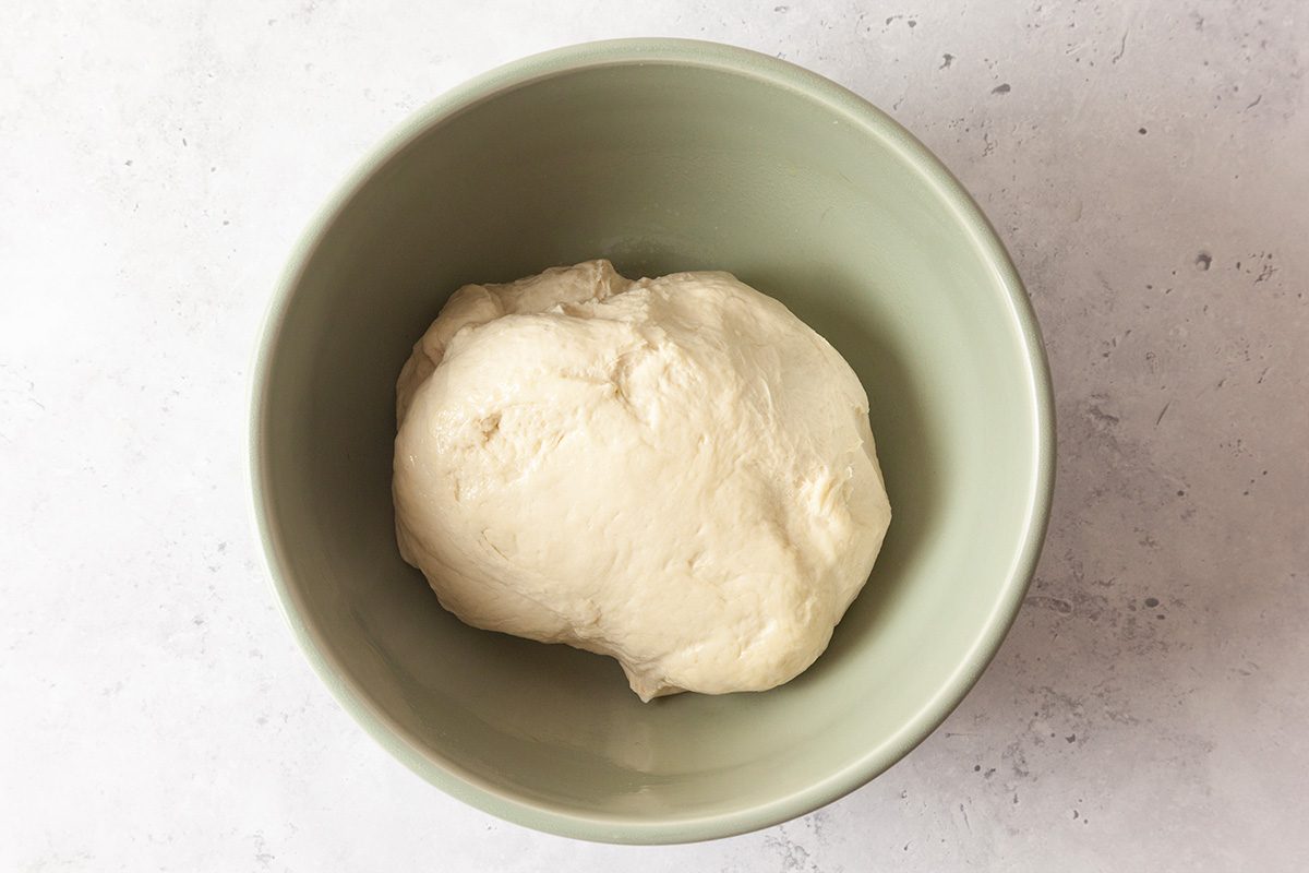 A ball of dough sits in a green bowl on a light, textured surface.