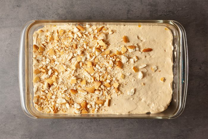 A rectangular glass dish filled with a creamy dessert topped with crushed cookies or crackers, sitting on a gray surface.