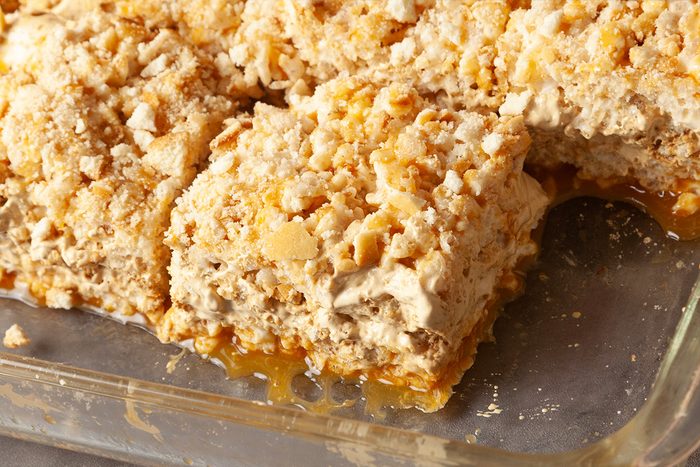 A close-up of a glass baking dish filled with squares of a crumbly dessert, possibly a caramel or nut bar, with a missing piece revealing a gooey layer underneath.