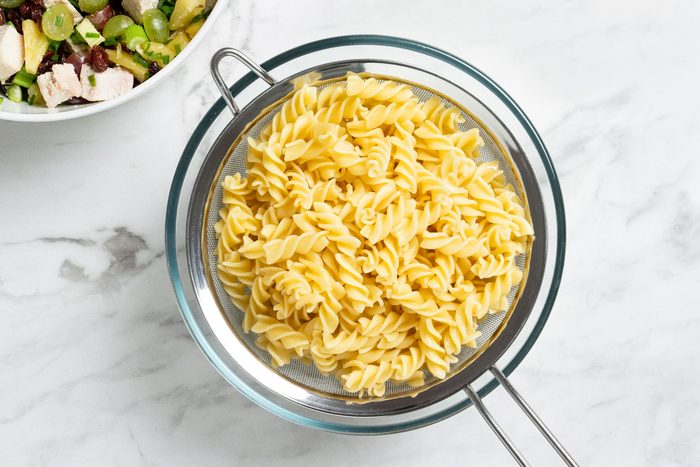 Overhead shot of cook pasta according to package directions; Drain pasta and rinse in cold water; all set on marble surface