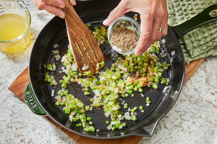 A person pouring seasoning into a pan of food.