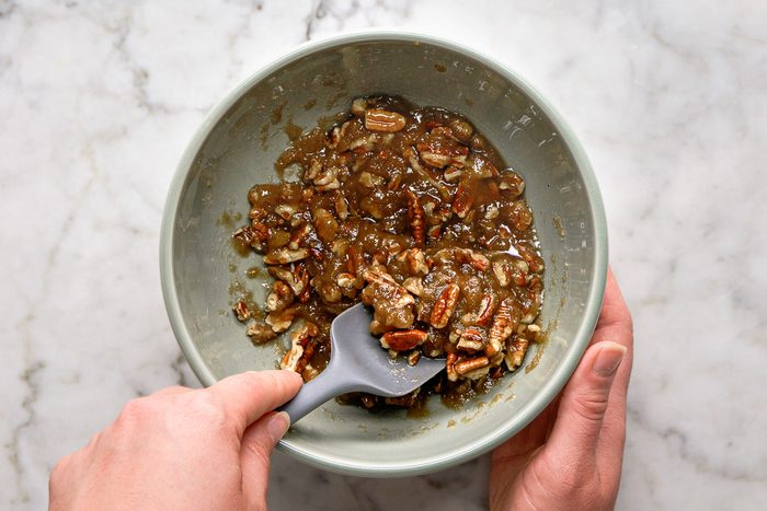 mixing melted butter with brown sugar and chopped pecans