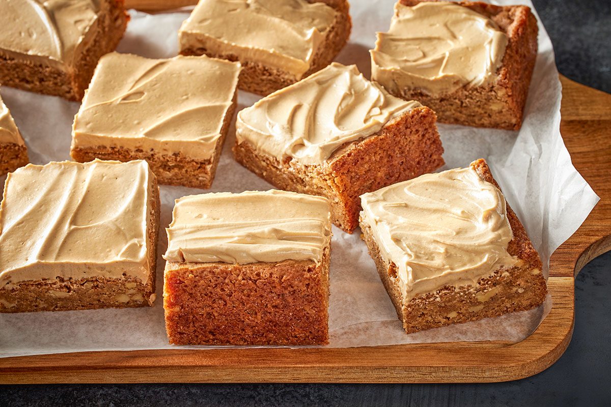 Close view shot of brown butter blondies topped with swirls of speculoos buttercream; arranged on parchment paper over a wooden board;
