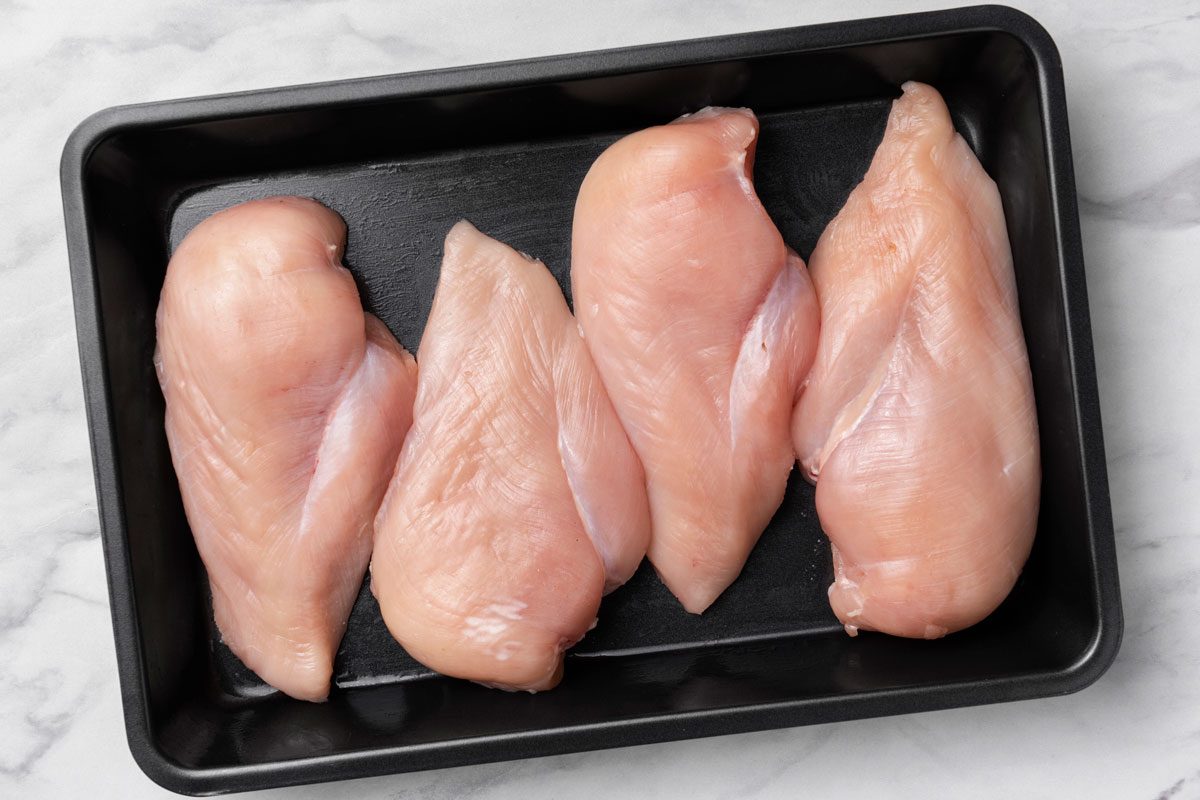 Overhead shot of place chicken in a greased shallow baking dish; all set on a marble surface;