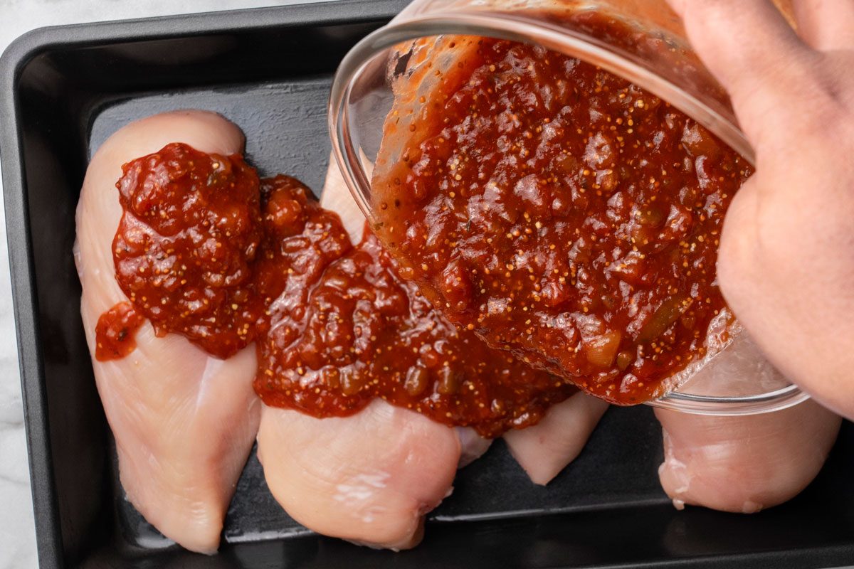 Overhead shot of pour mixture over chicken; all set on a marble surface;