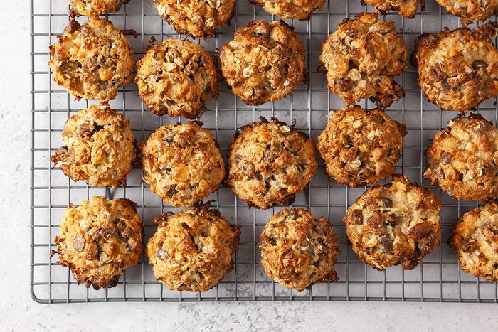Freshly baked oatmeal cookies with chocolate chips cooling on a wire rack, arranged in neat rows on a light-colored tabletop.