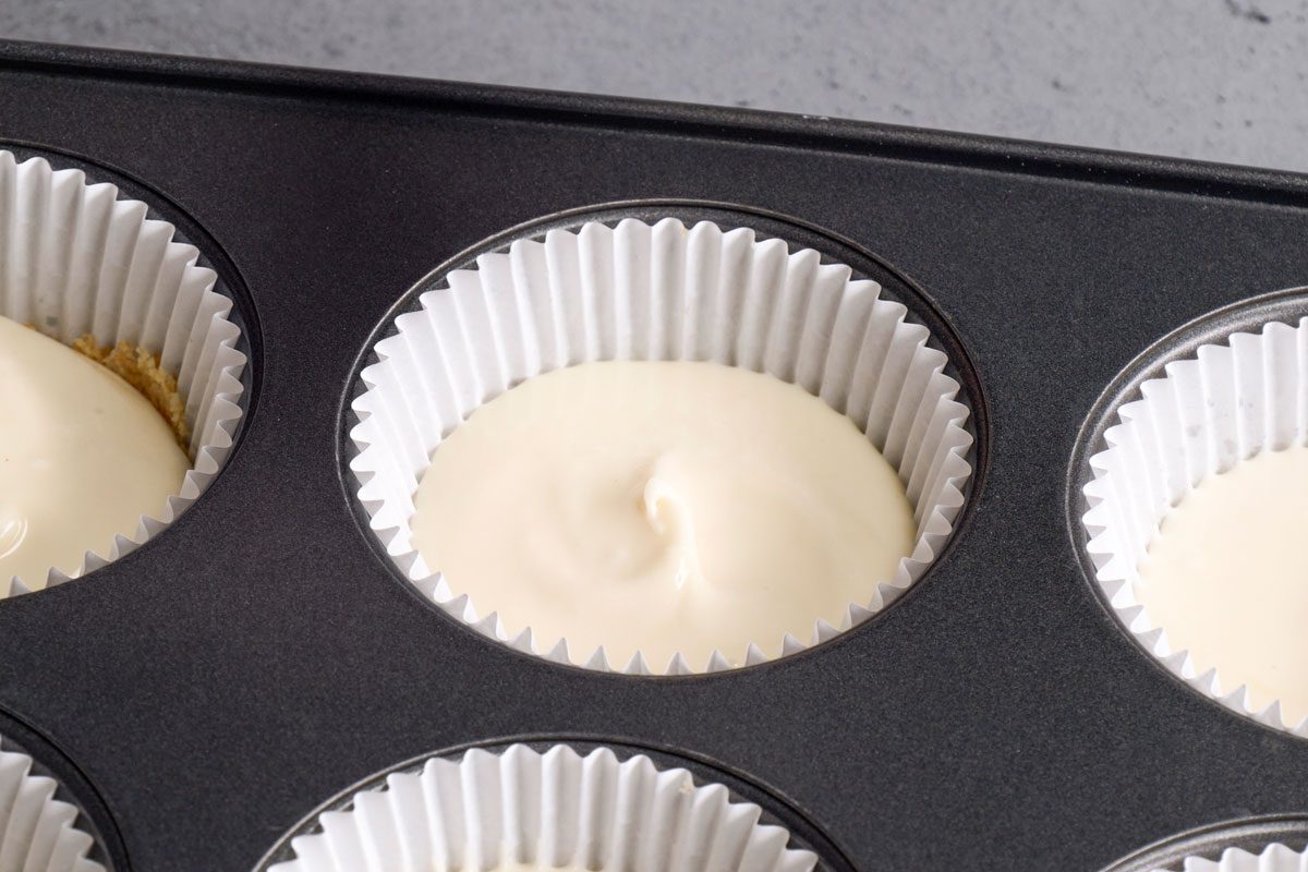 Closeup shot of a muffin tin with cupcake liners filled with smooth, pale batter, ready to be baked, The surface of the batter is creamy and even