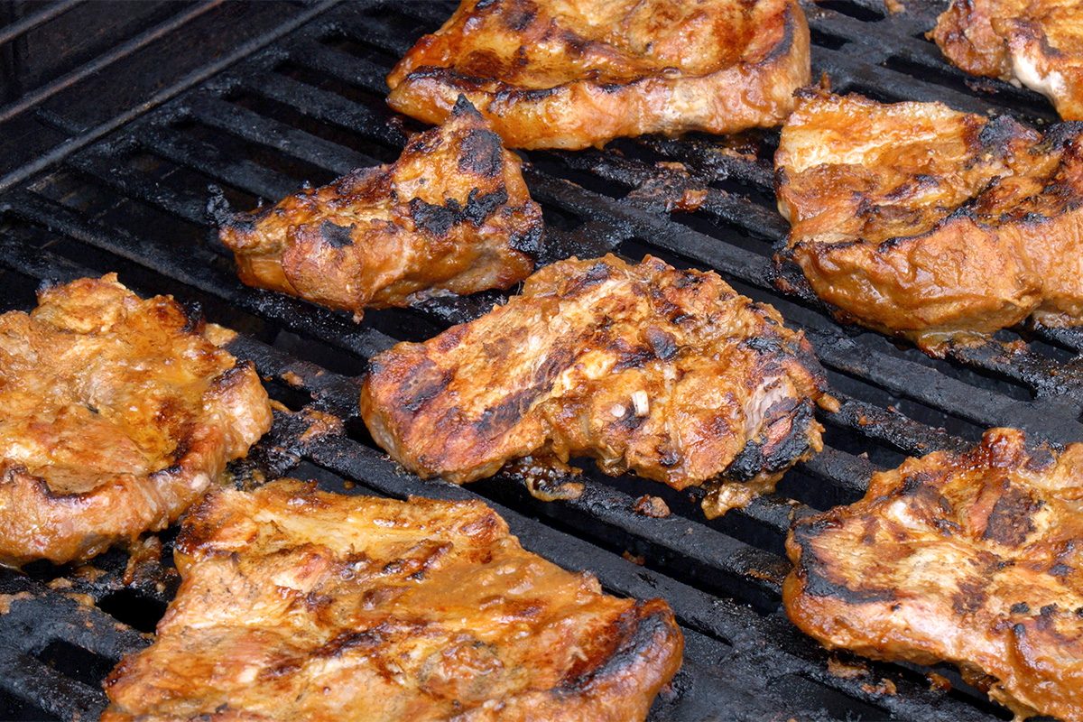 Several pieces of marinated and grilled meat are cooking on a barbecue grill, showing char marks and a golden-brown, slightly crispy exterior.