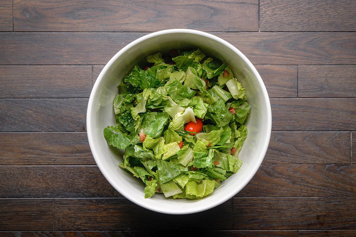 A white bowl filled with chopped romaine lettuce and a few cherry tomatoes sits on a dark wooden surface.