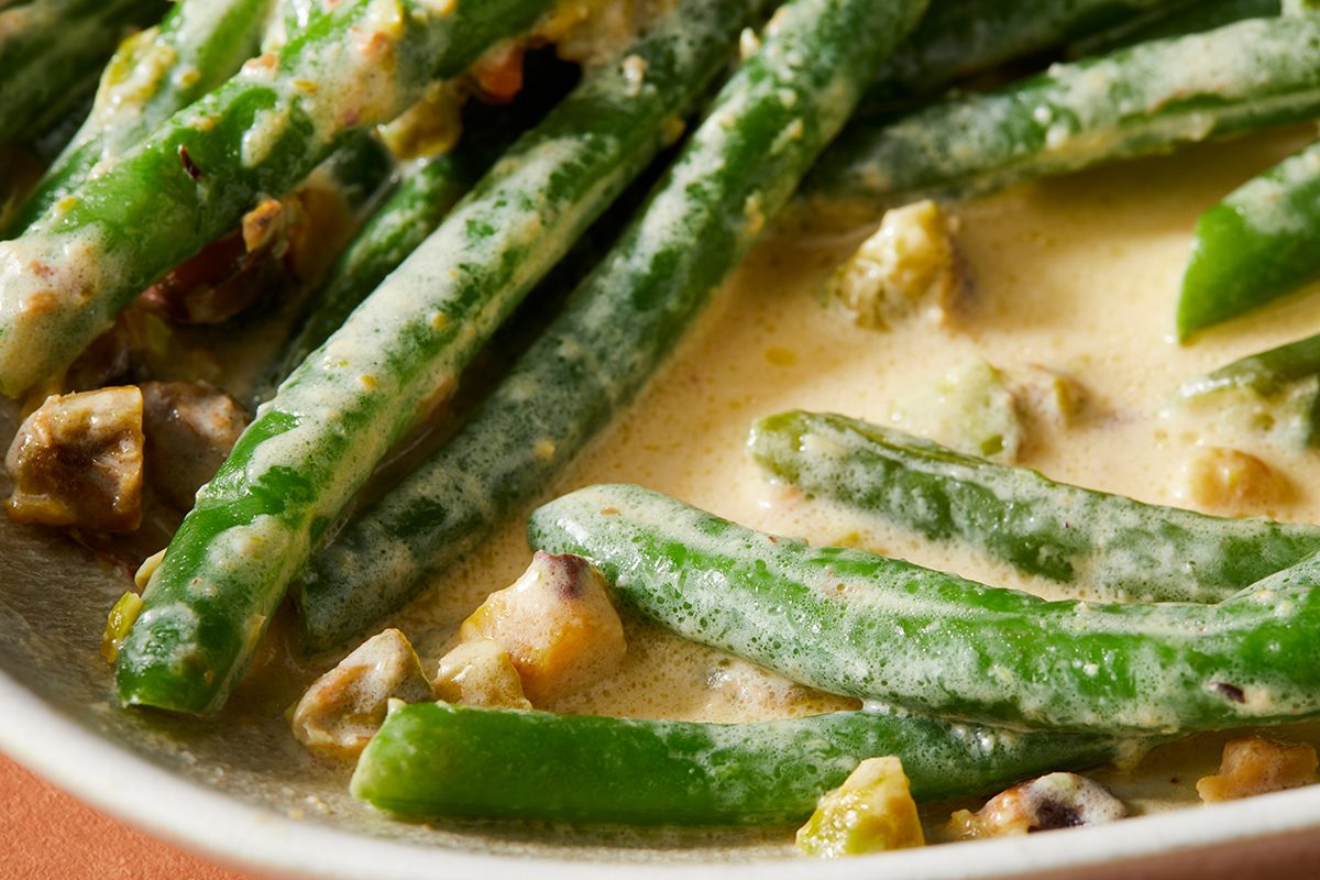 Close-up of green beans coated in a creamy sauce with chopped nuts, served in a dish.