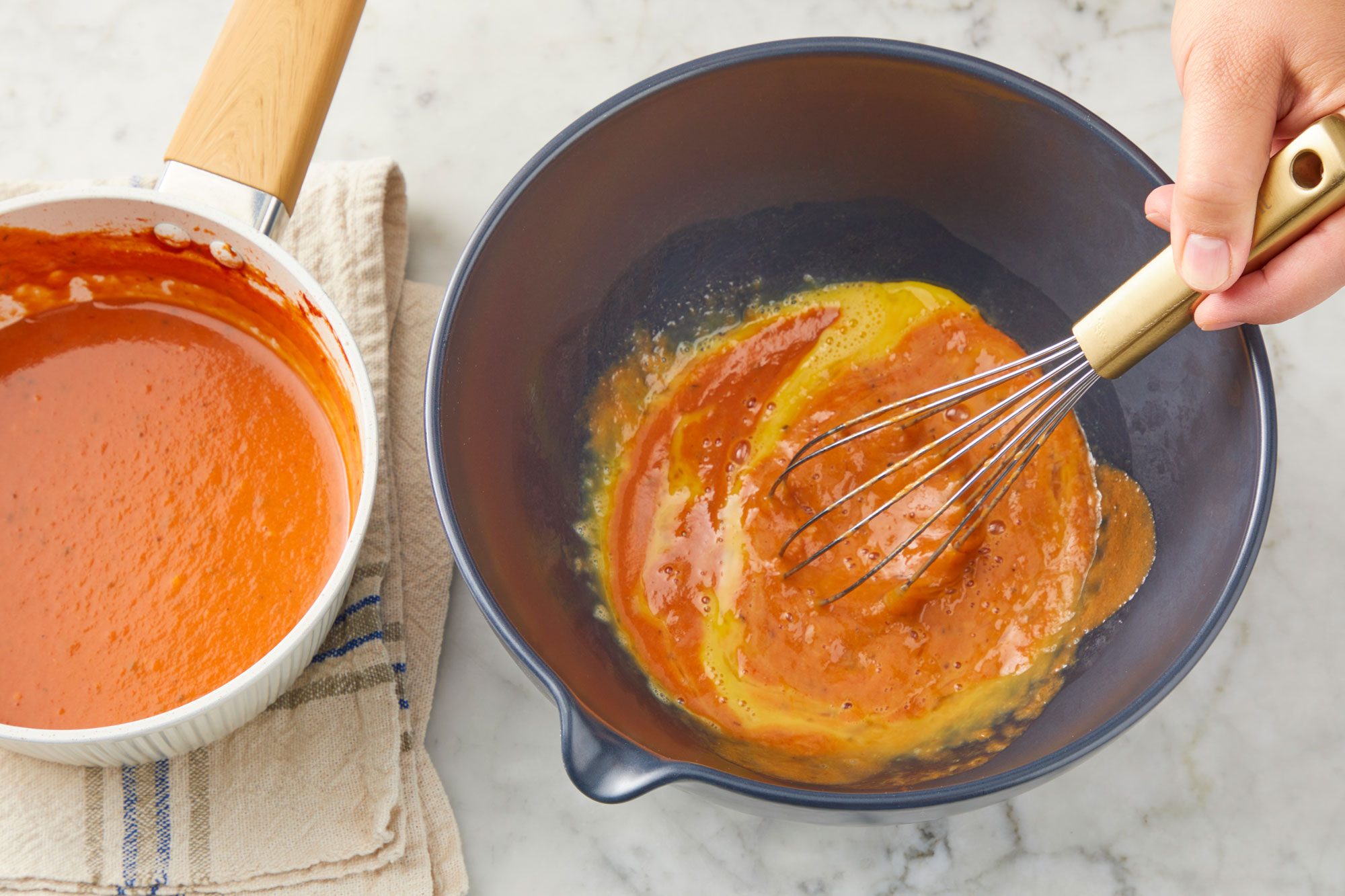 Overhead a large bowl whisk eggs; gradually whisk in a third of the milk mixture; Stir in the remaining milk mixture; whisk tool; all set on a marble surface;