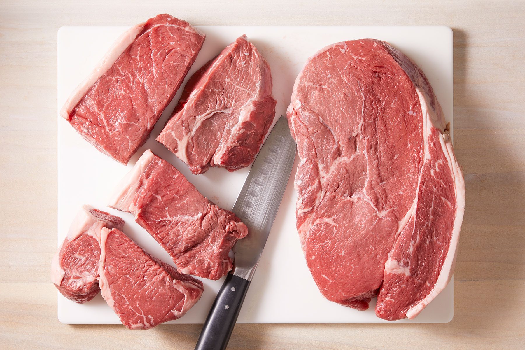 Cutting each steak into four pieces with a knife on white cutting board.