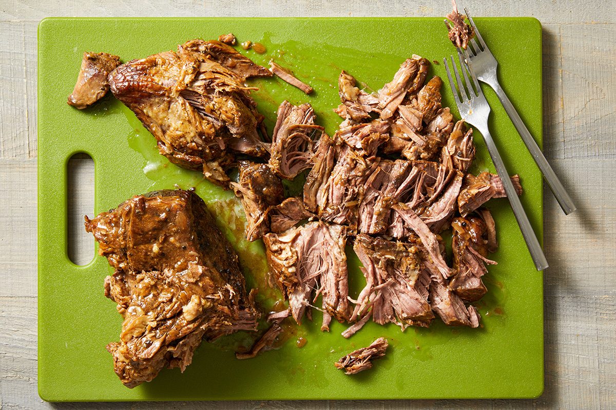 Overhead shot of cooked beef roast on a cutting board being shredded with two forks.