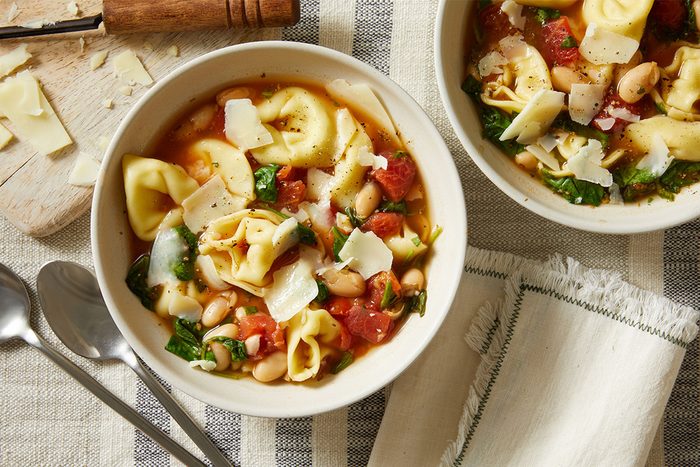 Overhead shot of two bowls of Christmas Tortellini & Spinach Soup, Spoons rest beside the bowls