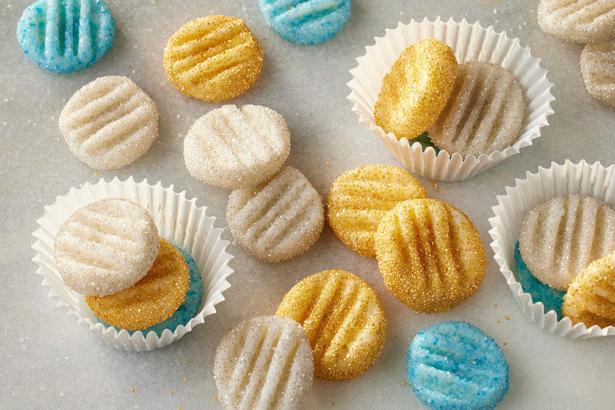 Overhead shot of round Cream Cheese Candies in gold, white, and blue, sugar-coated with fork marks