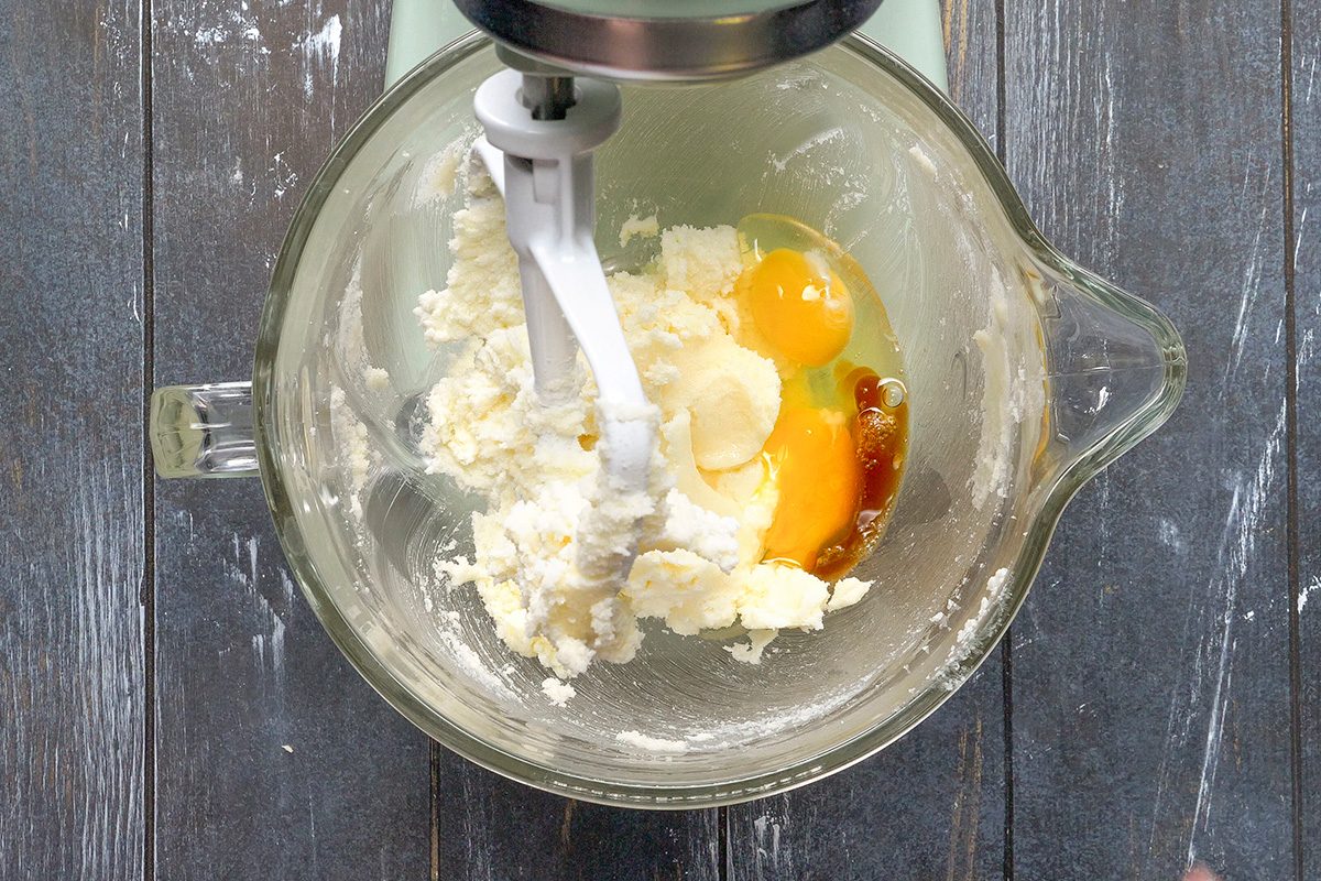 Overhead shot of a glass mixing bowl containing butter, sugar, eggs, and vanilla extract being mixed with a stand mixer