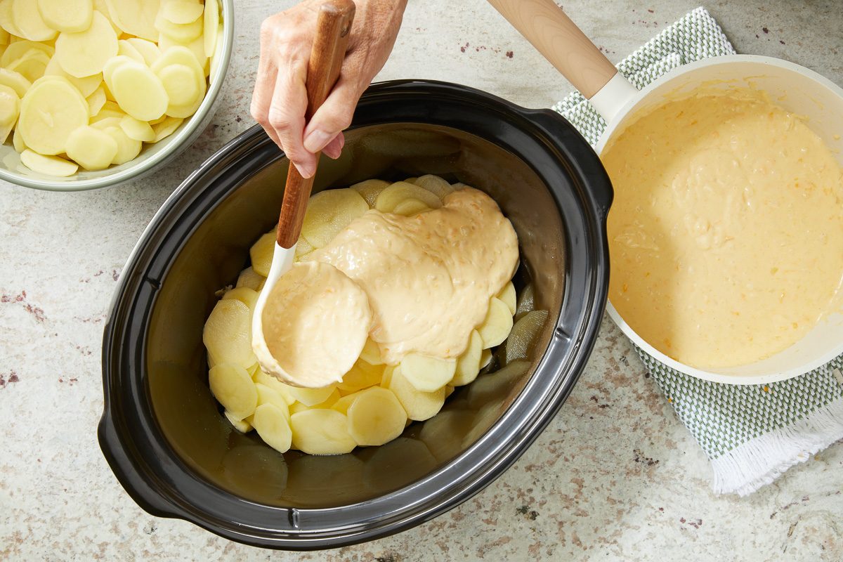 cheese mixture being poured over layer of potatoes