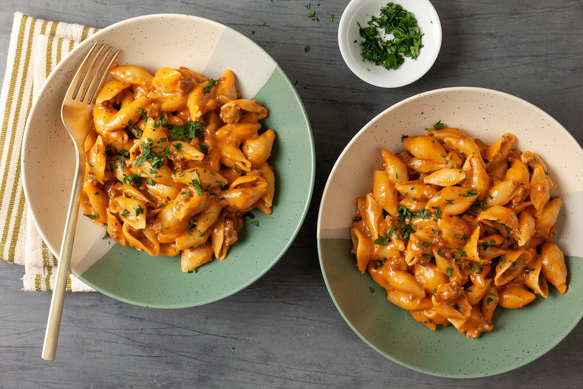 Overhead shot of a Homemade Hamburger Helper pasta shells are served in creamy orange sauce with parsley on top on a gray surface and a gold fork is on one bowl