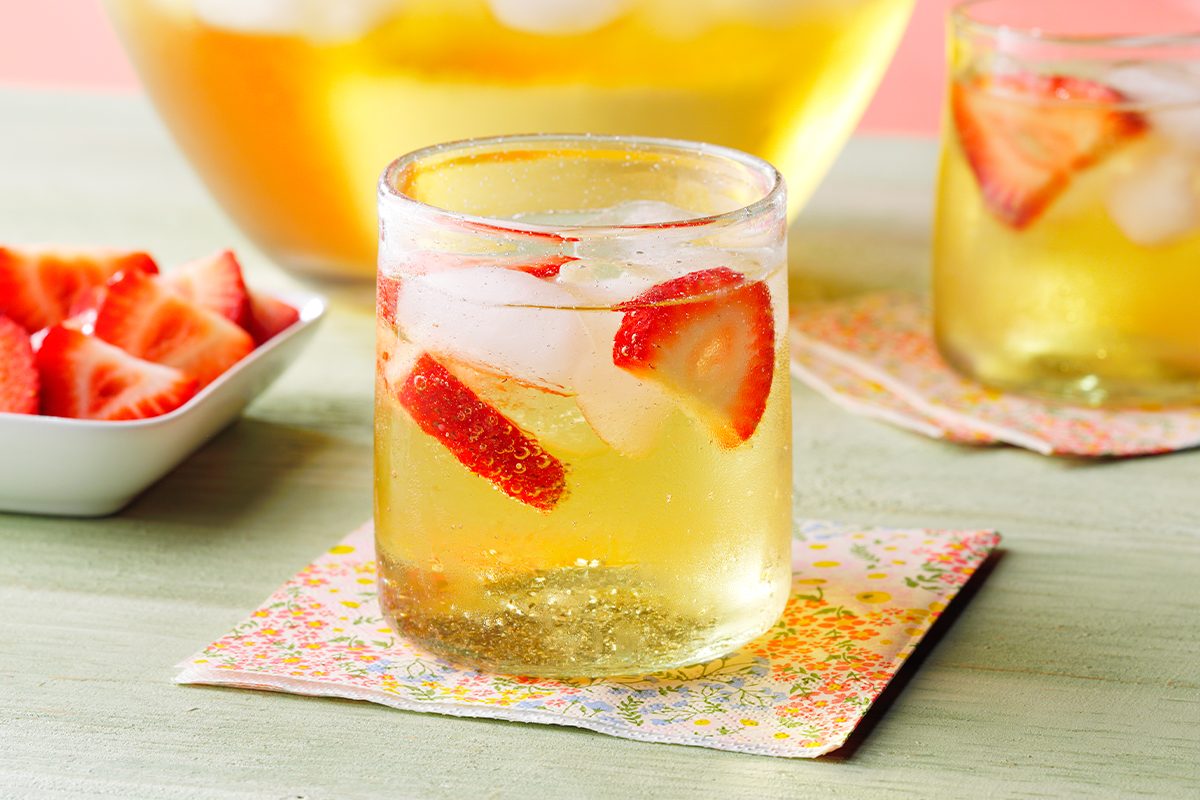 Side view of Mock Champagne Punch kept on top of a table coaster next to garnishes on a green table.