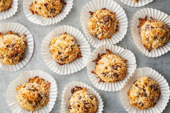 Overhead shot of several Almond Joy Cookies with chocolate chips in white paper liners, arranged on a gray surface;