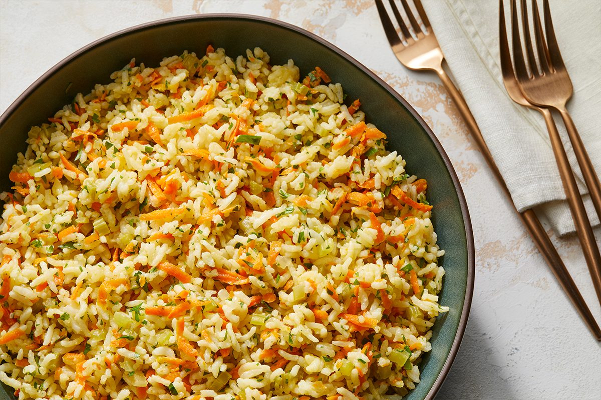 Overhead shot of Baked Rice Pilaf in a large bowl; forks and a napkin are nearby on a marble surface;